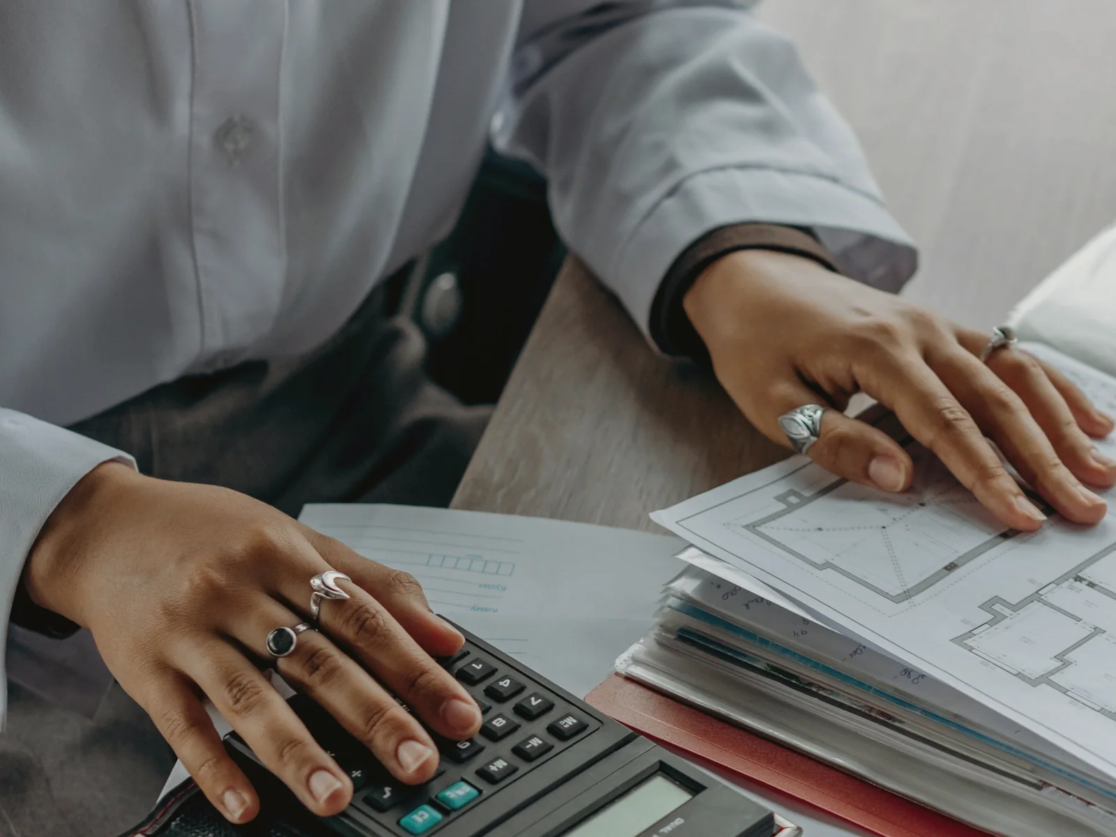 Hands reviewing a printed plan beside a calculator and folders