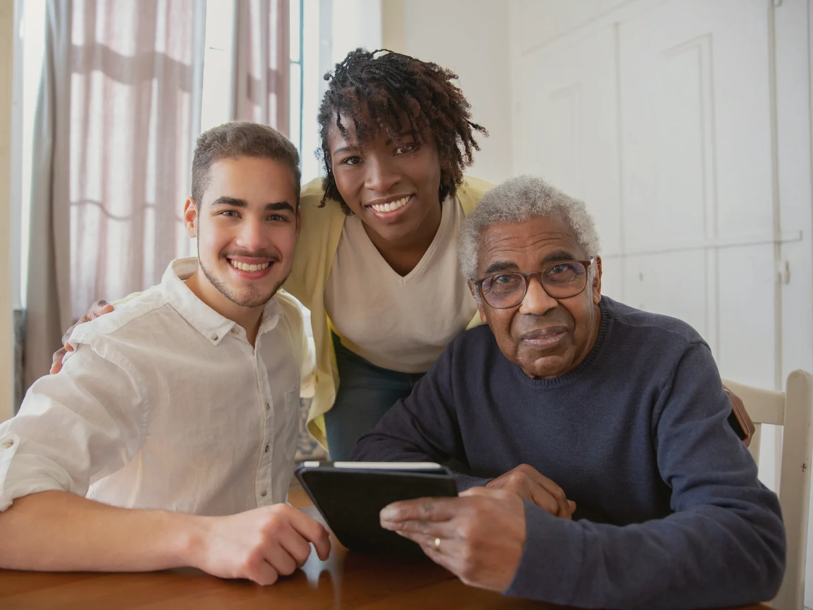 Older adult and two guests looking at a tablet together